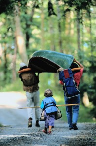 Parents walking with canoe and child behind them